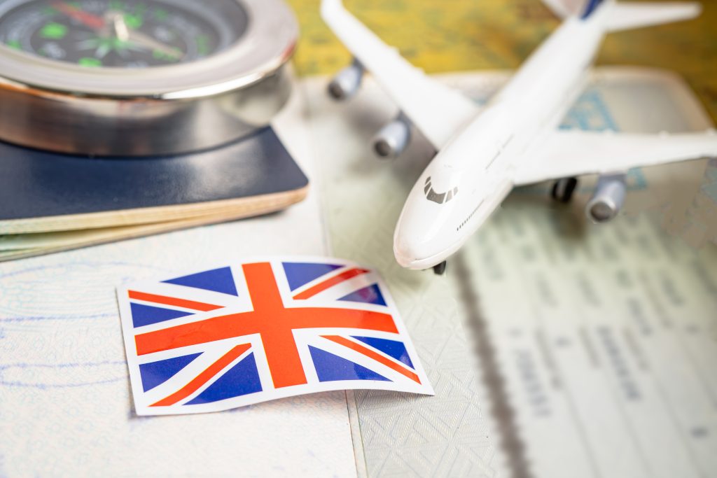 Union Jack stickers on a white surface with a small white toy airplane and a compass nearby, suggesting travel planning.